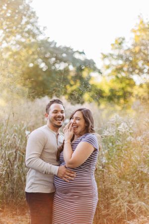 Couple laughing together in sunlit meadow with tall grass.