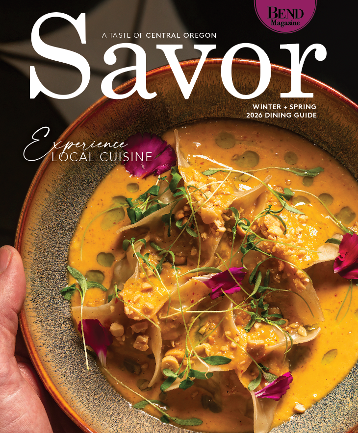 A vibrant Thai curry dish garnished with edible flowers and microgreens in a dark ceramic bowl.