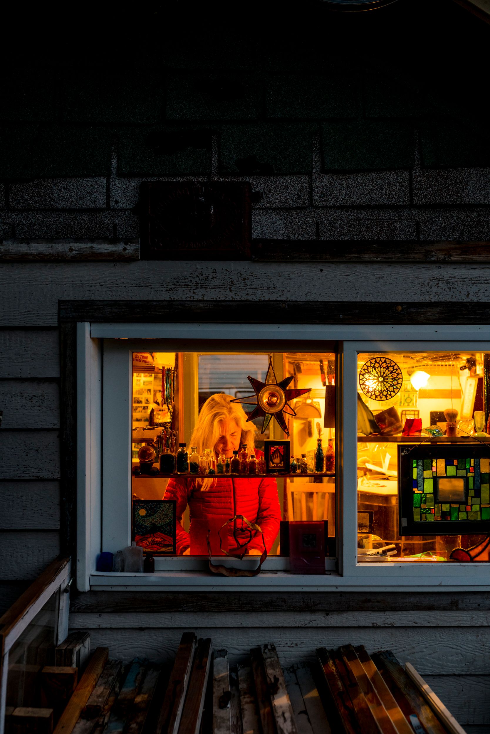 A cozy window display glows warmly at night with nautical decor and antiques illuminated by soft yellow lights.