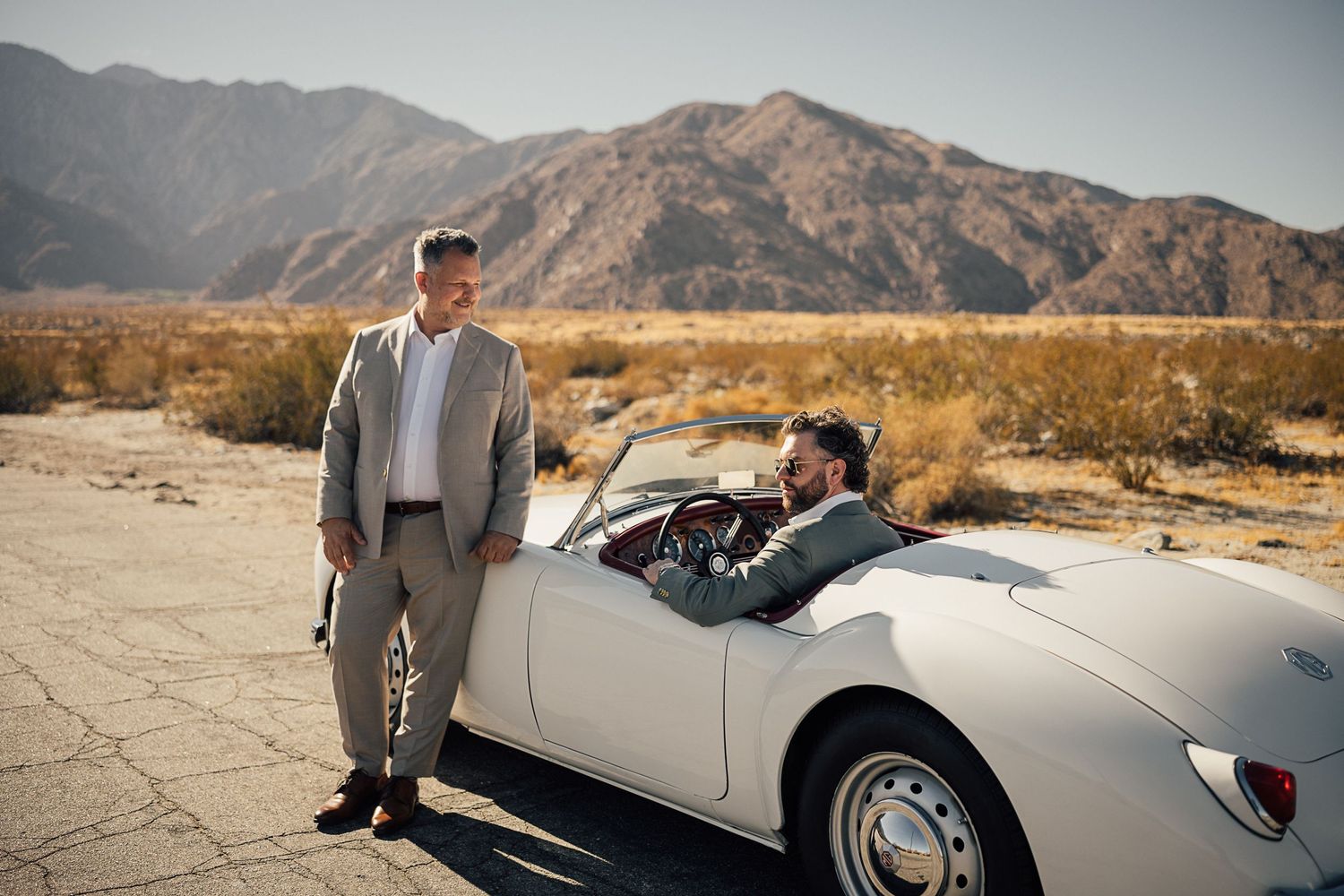 Vintage white convertible car parked in desert landscape with mountain backdrop.