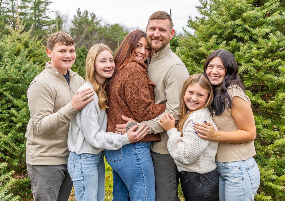 A group shares joyful moments together while posing in front of evergreen trees during a photo session.