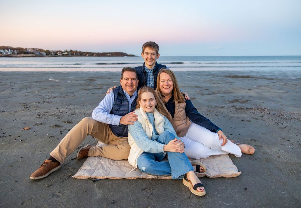 Family relaxing together on beach blanket during sunset photo session.