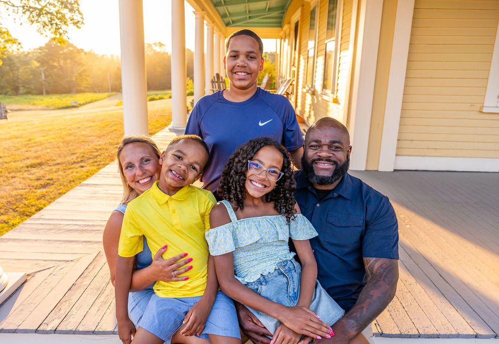 A family poses together on a front porch during golden hour sunlight.