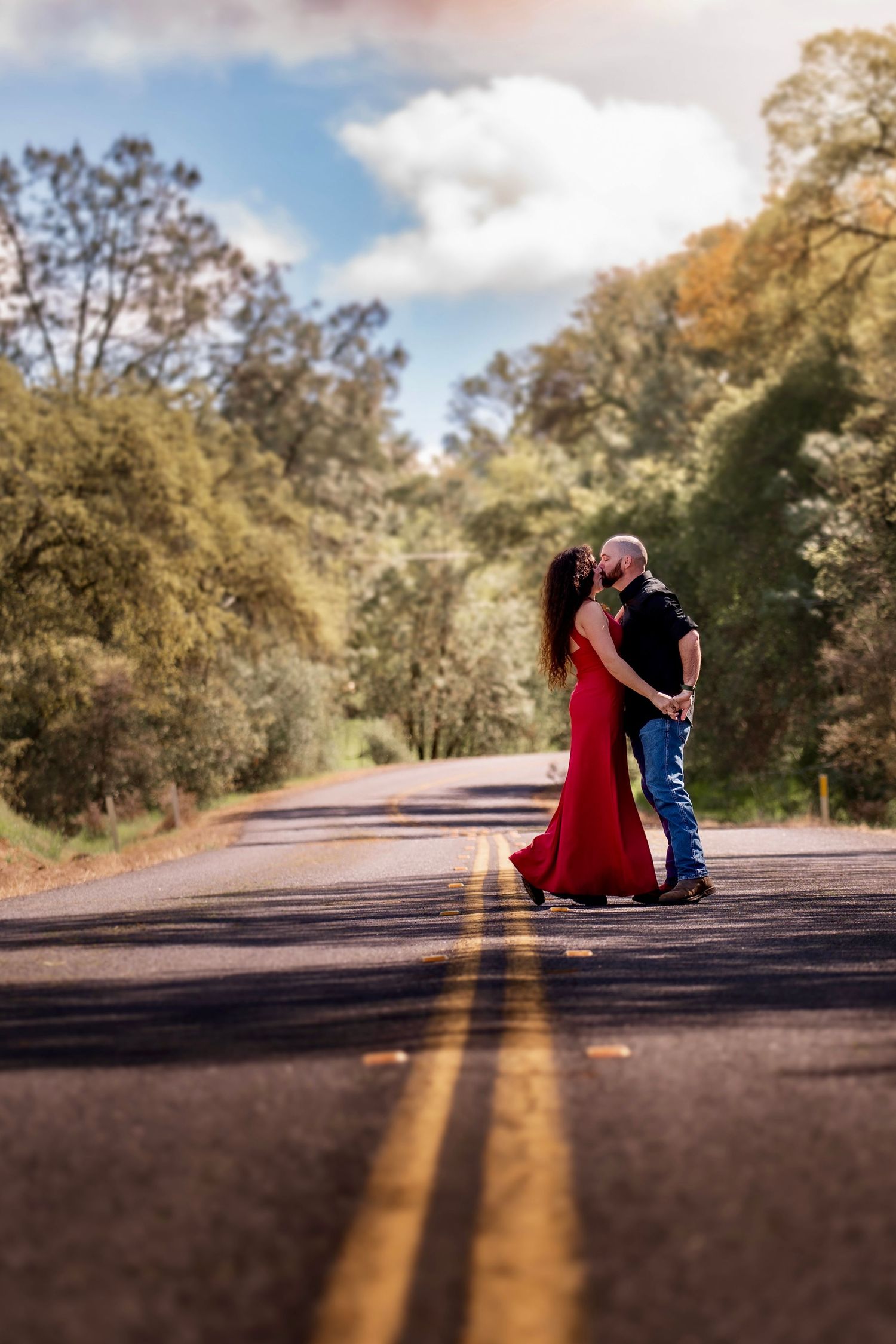 A husband and wife in a red dress dance together on a country road