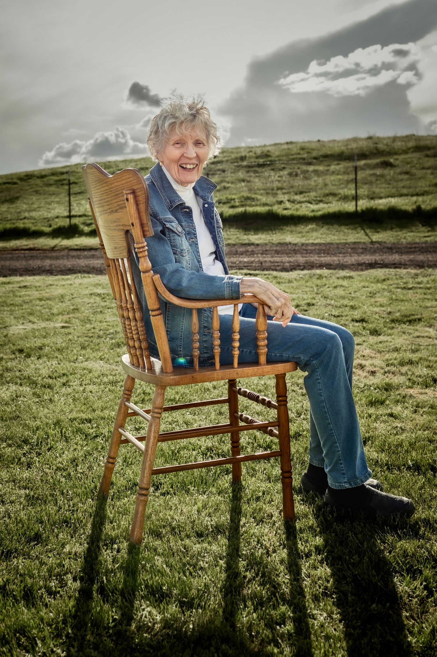 A great grandmother sitting happily in wide open green pasture as the sun goes down