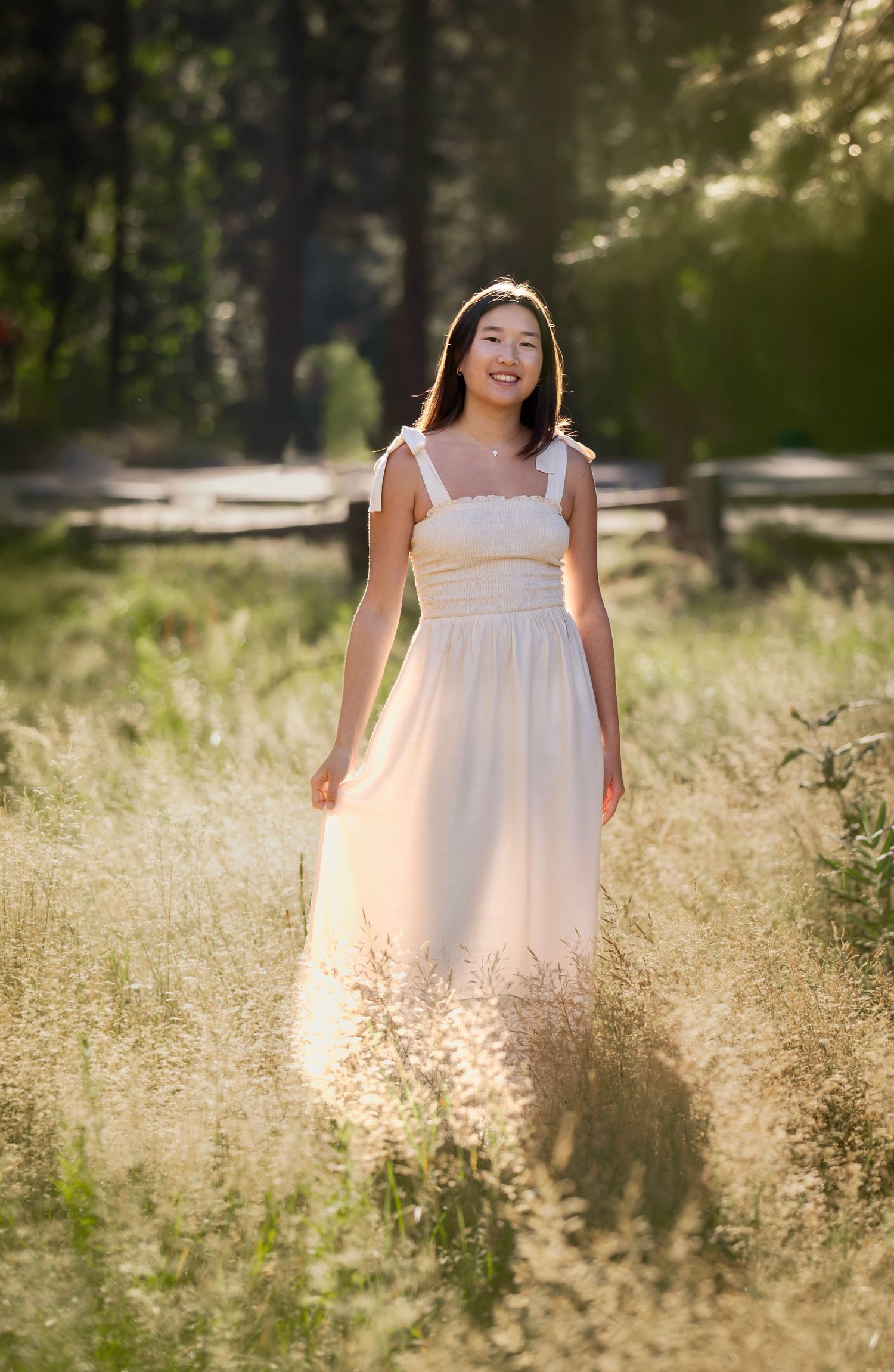 A girl smiles in a dreamy white dress, in the soft sunrise during her senior session in Yosemite