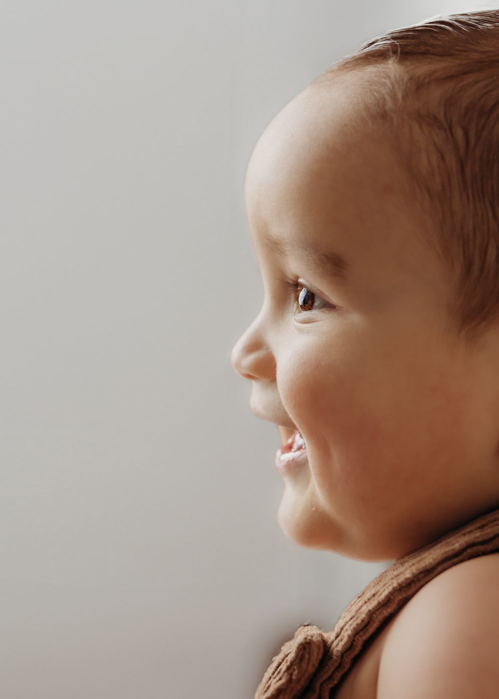 A series of close-up profile shots showing a smiling baby cradled in brown blanket against a light background.