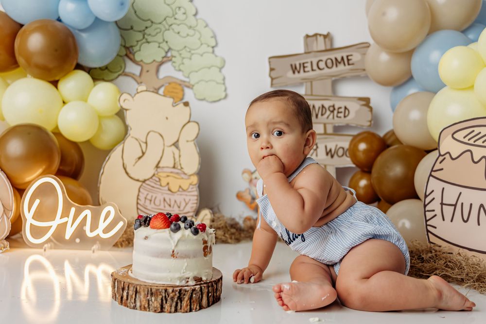 First birthday photo collage backdrop with rustic wood slices, balloons, and baby decorations shows milestone celebration setup.