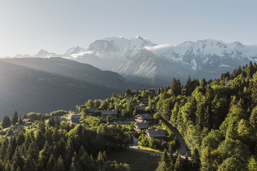 Aerial drone view of an alpine village surrounded by pine forest and mountain peaks — French Alps landscape photography — Paul Brechu