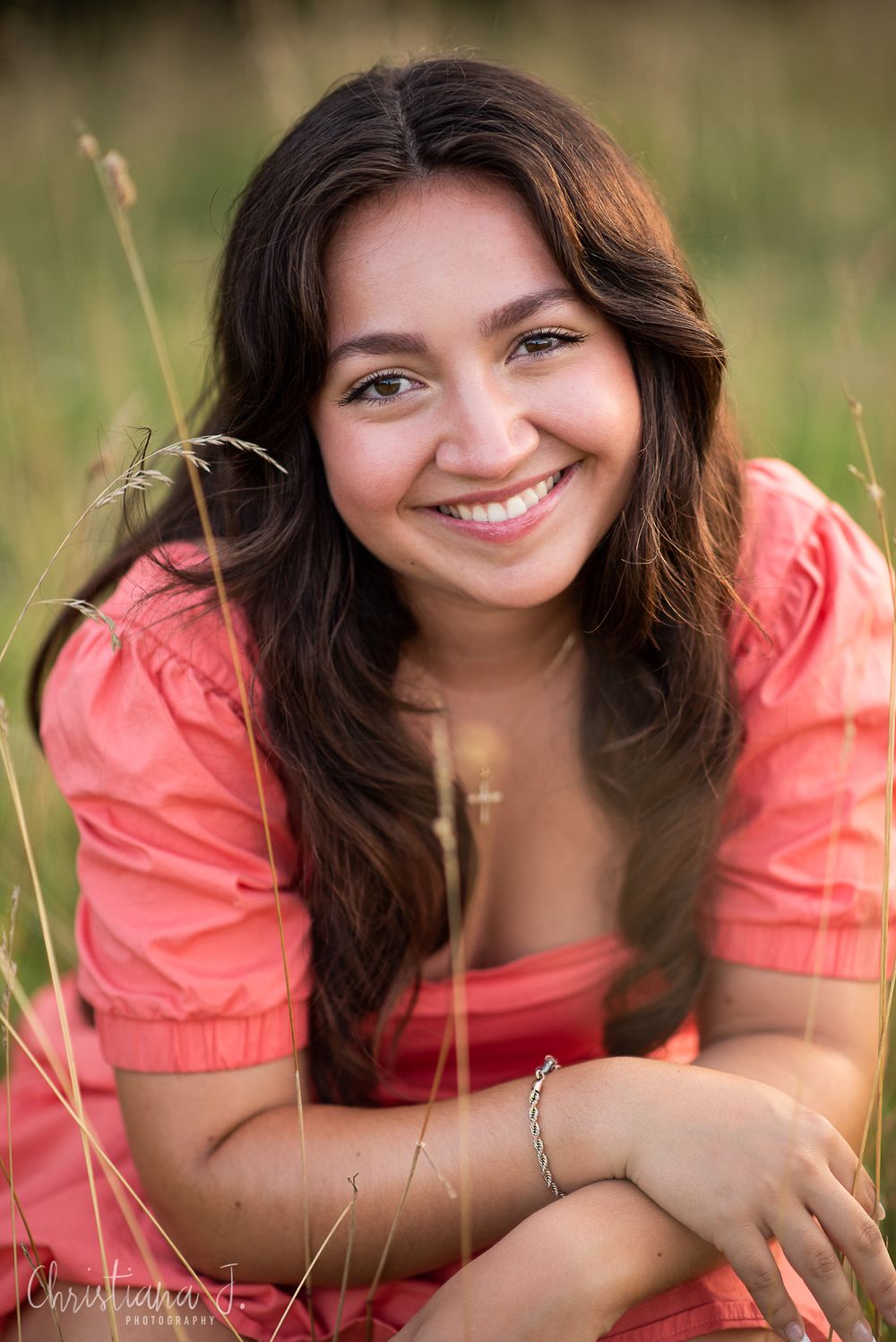 High school senior photographer Kansas City, Senior girl smiling in portrait with coral dress amid tall grass in natural lighting.