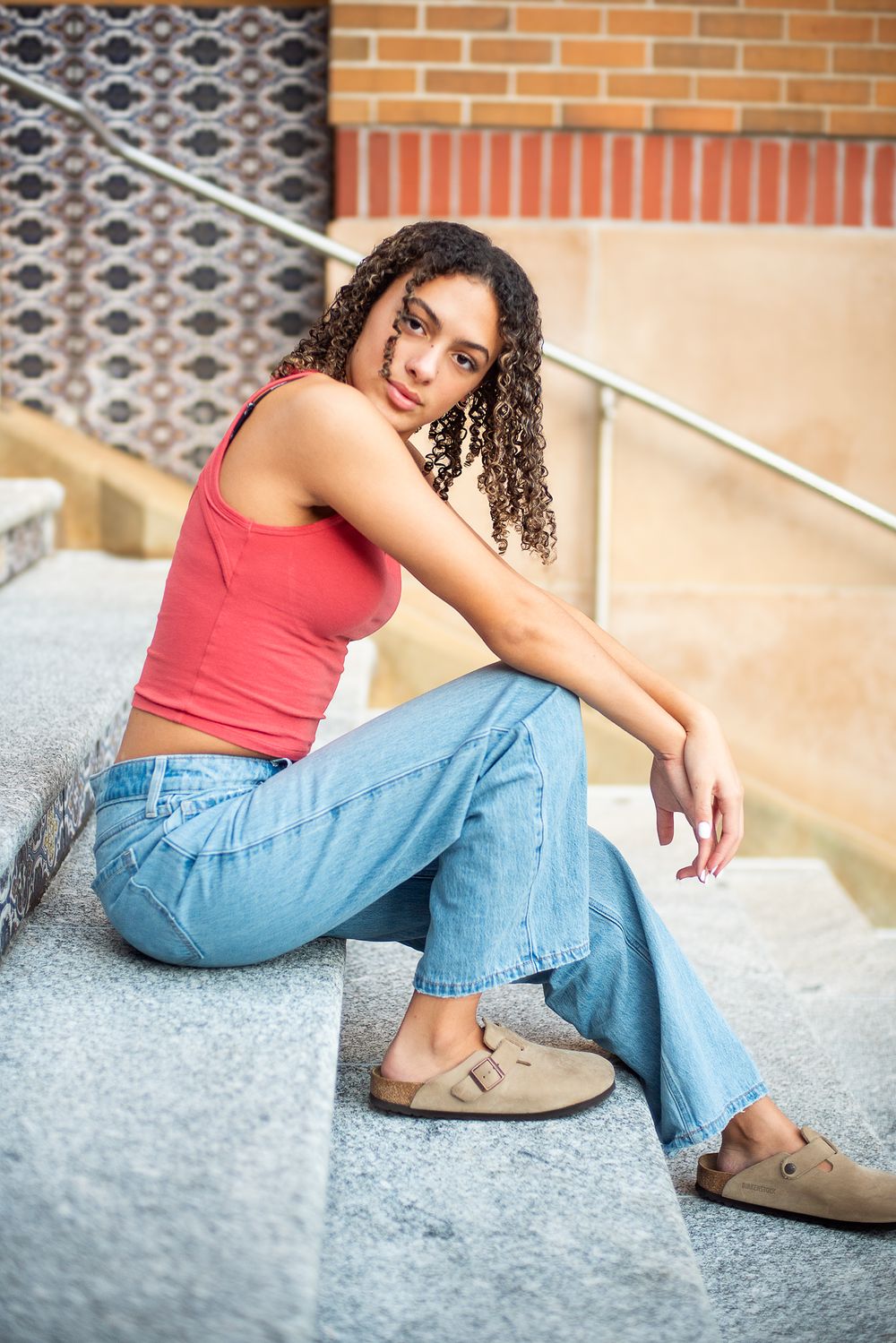 Casual portrait on concrete steps with person in red tank top and relaxed denim.