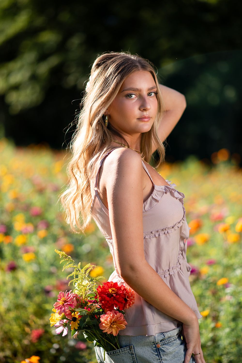 Portrait in a flower field wearing pink top with red bouquet in warm sunset light.
