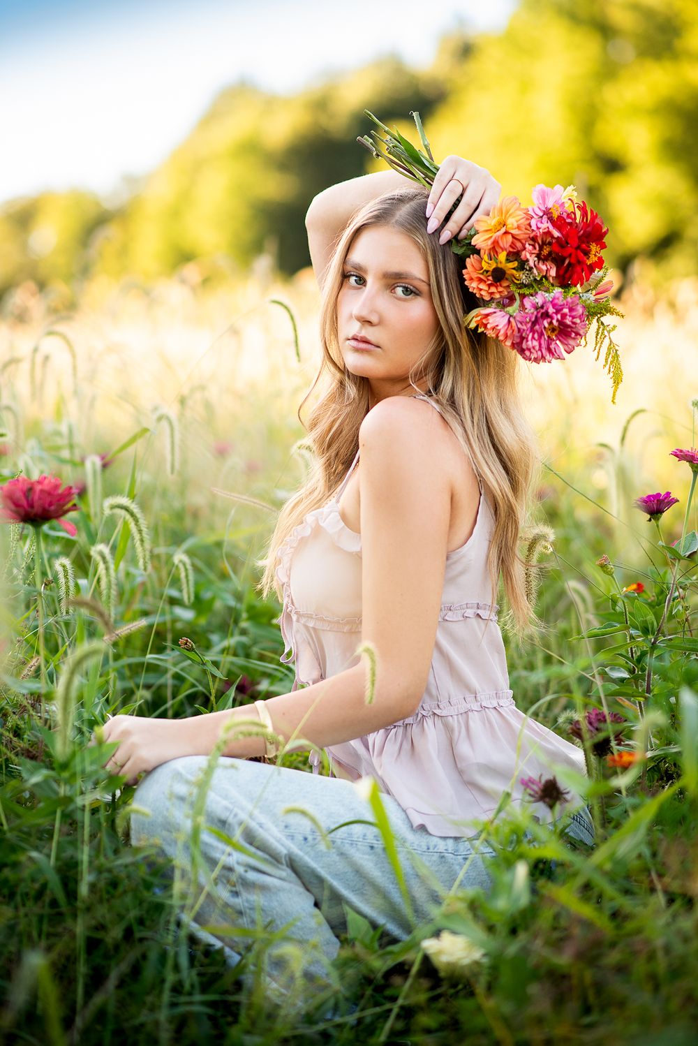 golden hour photoshoot high school senior girl in flower field holding a bouquet over head with soft light and tall grasses kansas city