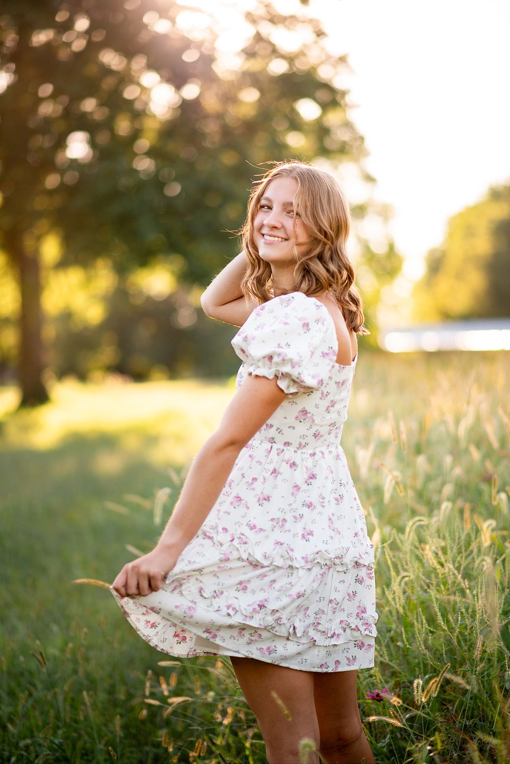 high school senior girl wearing a white summer dress walking naturally at wildflower field in kansas city missouri during golden hour