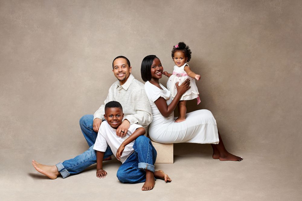 A joyful Black family of four poses together in a professional studio portrait with neutral beige background.