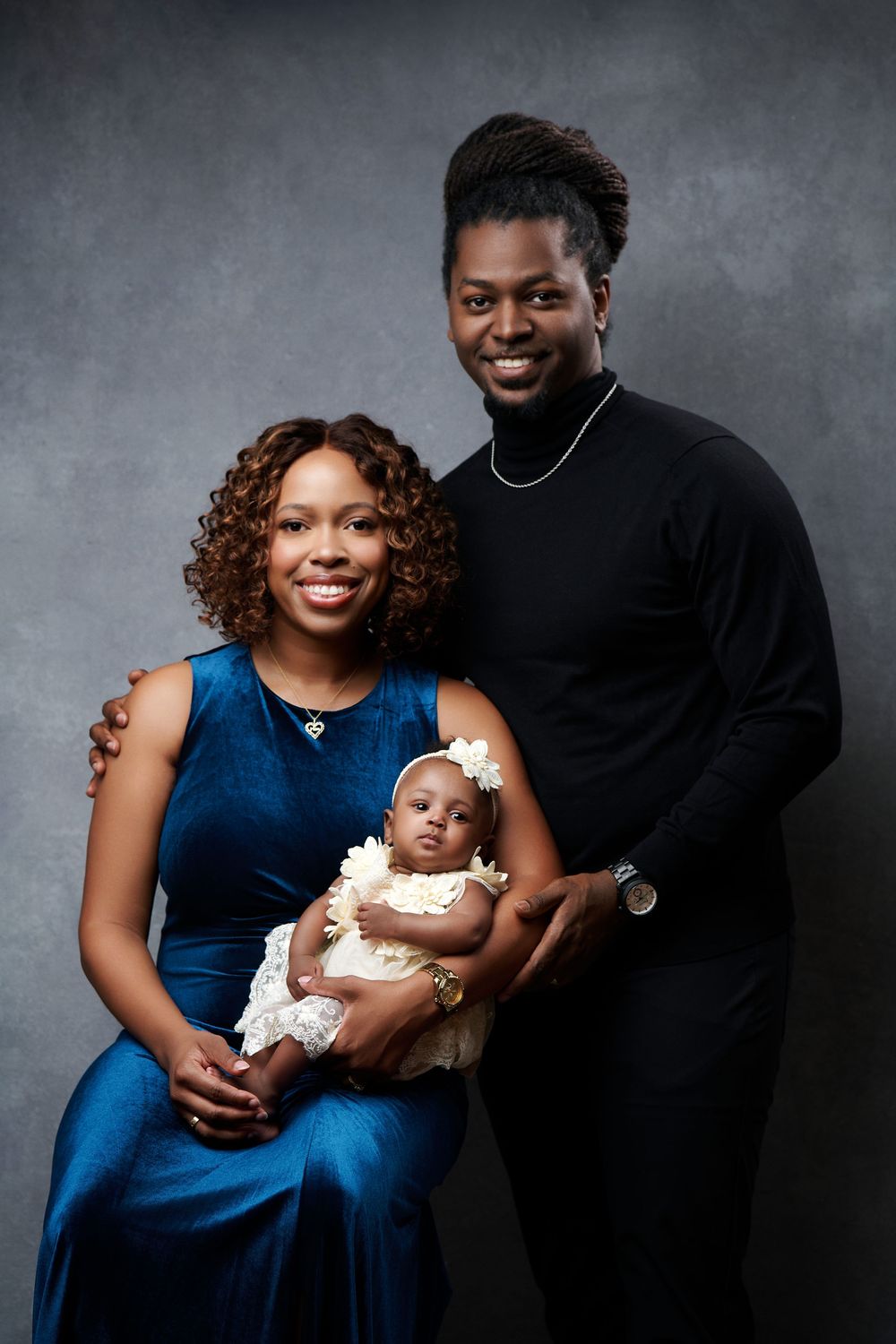 A family of three poses for studio portraits wearing blue and black against a dark gray backdrop.
