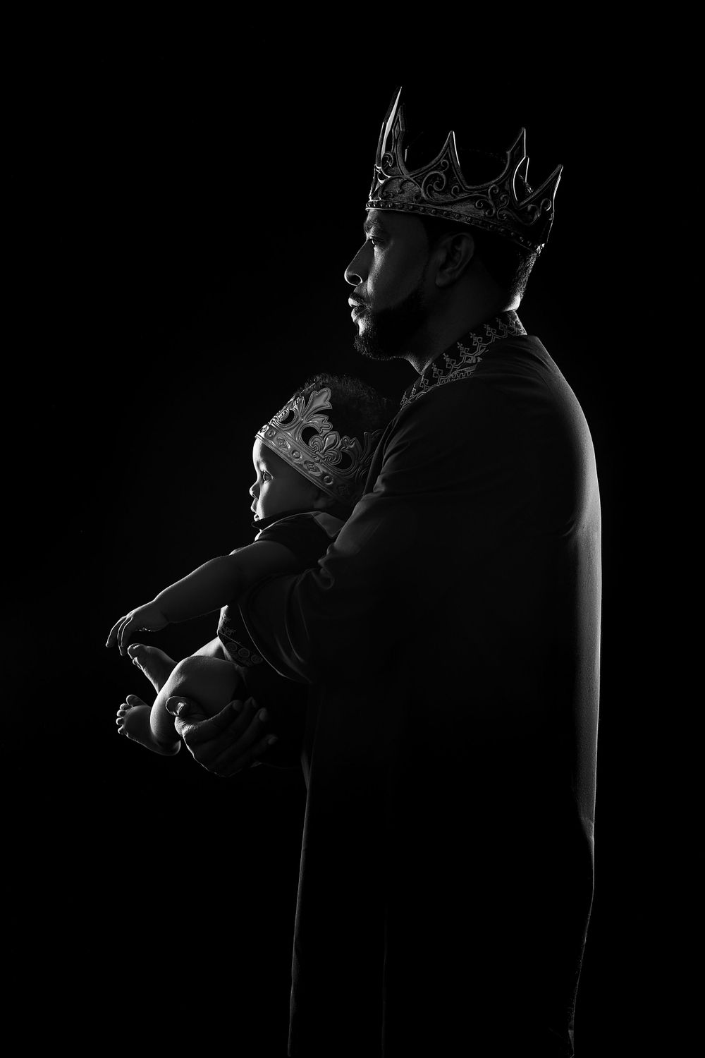 A dramatic black and white profile silhouette of a person wearing a dark crown and cloak against a black background.