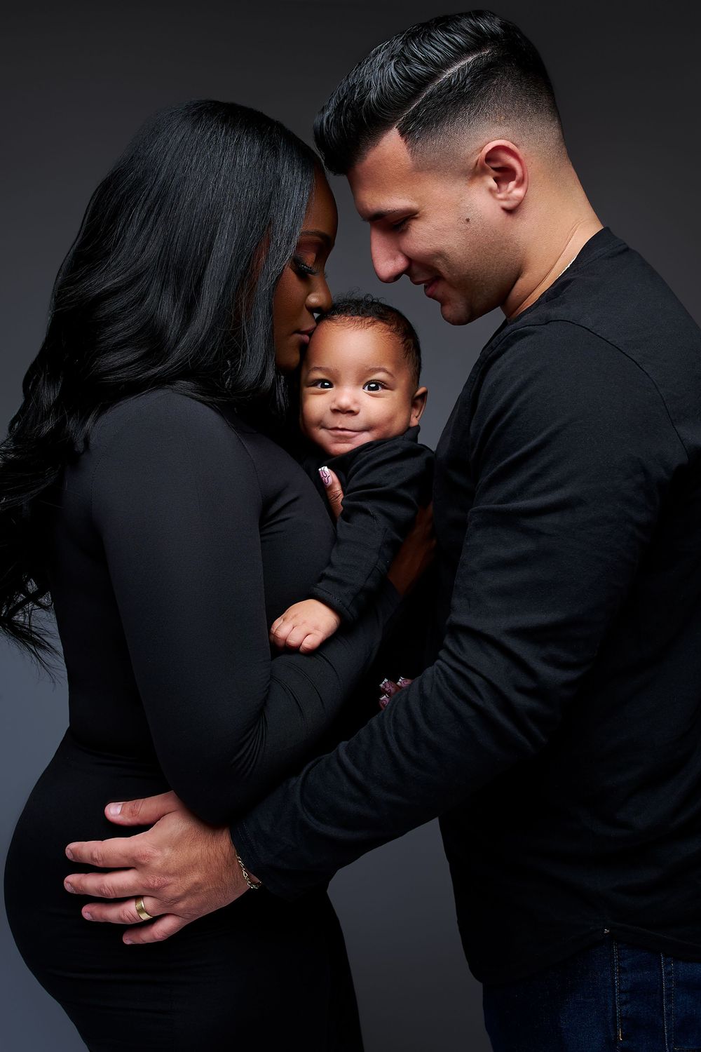 Intimate maternity photo series showing a couple in black clothing against dark background sharing tender moments.