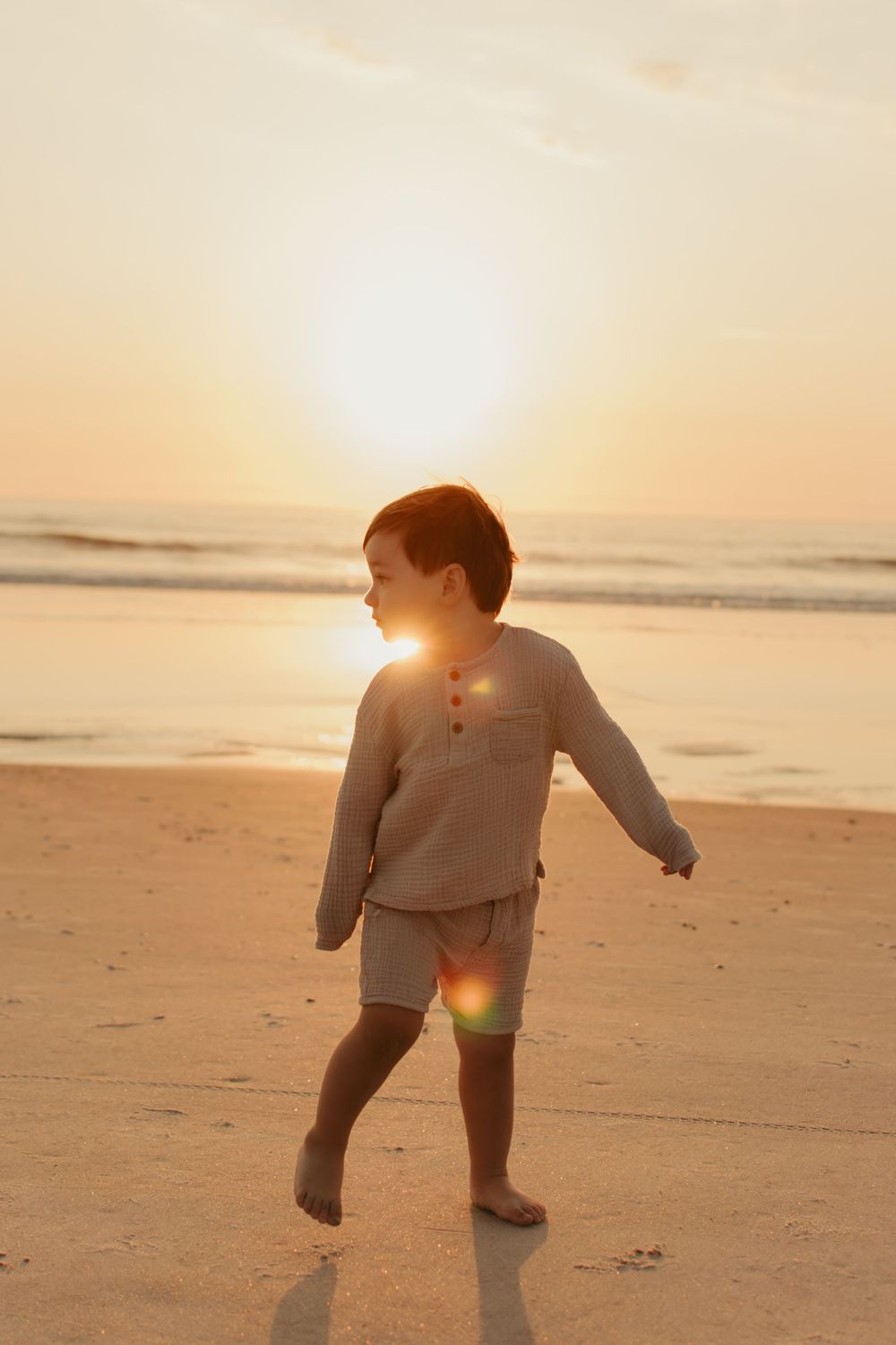 Child playing on beach at golden hour with sun creating beautiful backlight.