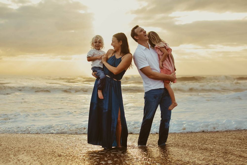 Family enjoying sunset together on a beach with waves and golden sky in the background.