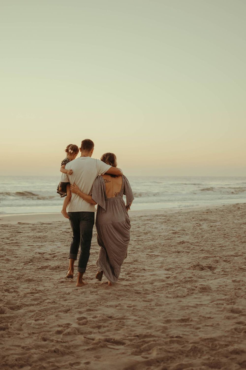 Group walking along sandy beach at dusk with ocean waves in background.