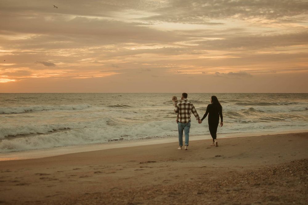 Silhouettes of people walking along a beach at sunset with dramatic orange and gold clouds.