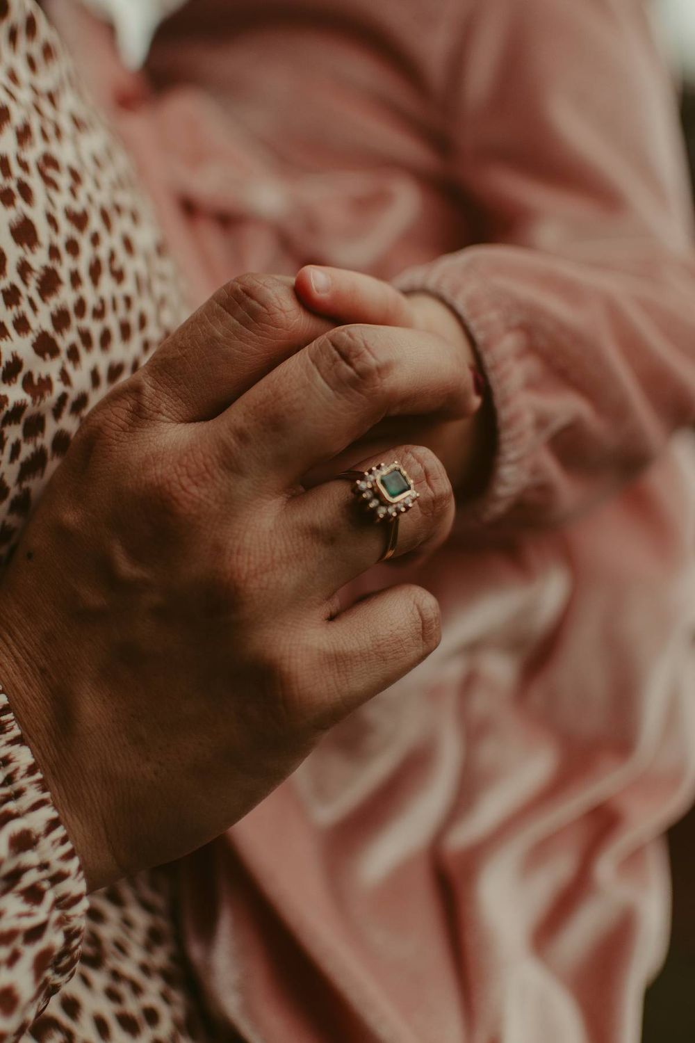 Close-up of hands with an engagement ring against a pink floral background.