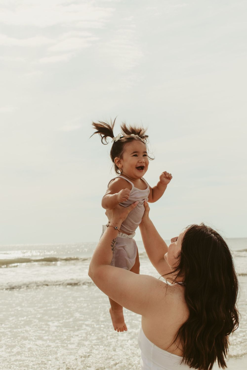 Joyful moment captured as baby is lifted high in the air at the beach.