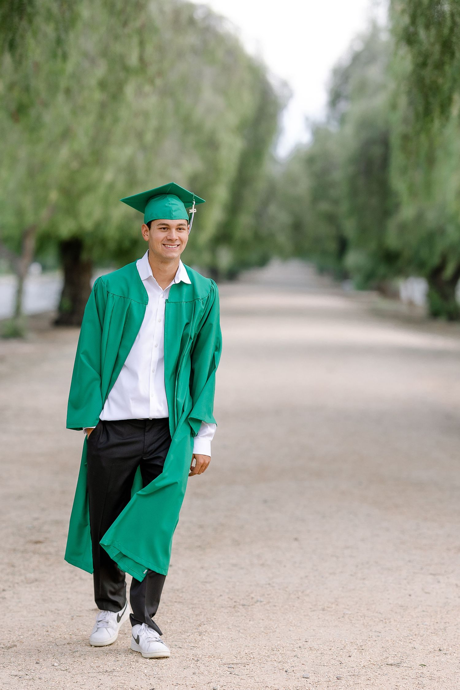 Handsome young man walking up tree lined street excited to go to graduation