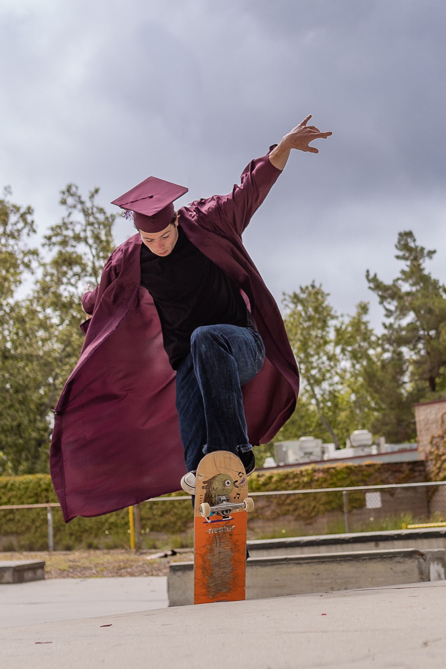 Claremont high school student in maroon cap and gown skateboard in air