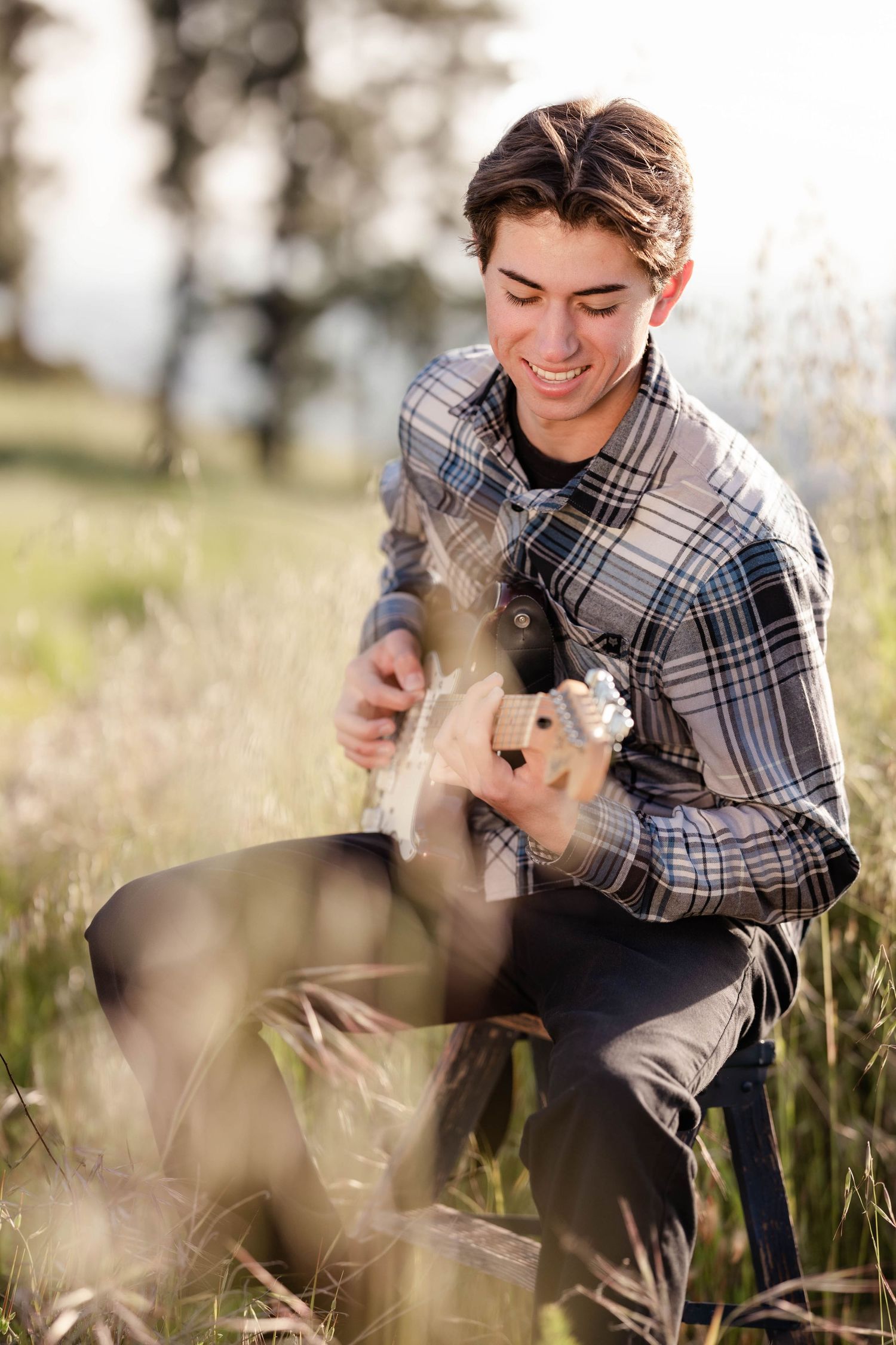 guy in flannel shirt playing guitar outside high school senior  fun phots session in a field