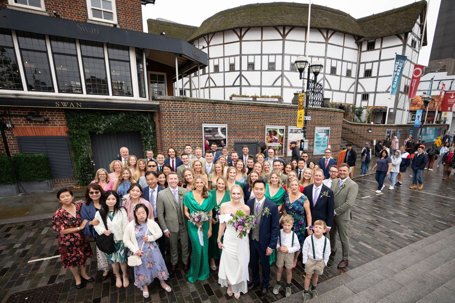 Large wedding group photo gathered outside the historic Shakespeare's Globe Theatre in London.