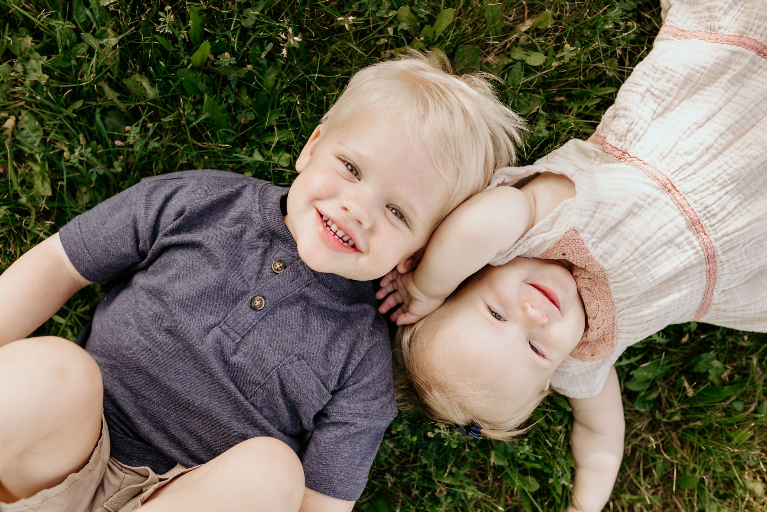 A family lies together on green grass during a warm summer day creating a candid outdoor portrait.
