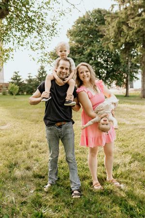 A playful family enjoys a fun moment together outdoors on a grassy hill during a sunny summer day.