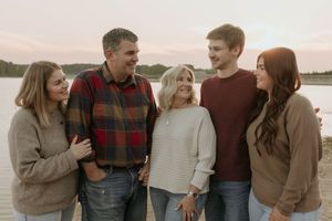 Group laughing together outdoors by a lake during sunset wearing cozy fall sweaters and plaid.