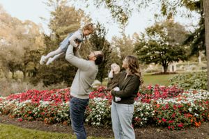 Playful family moment in garden with blooming red and white flowers.