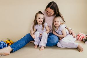 Mother and daughters in casual attire sharing intimate moment on studio floor.