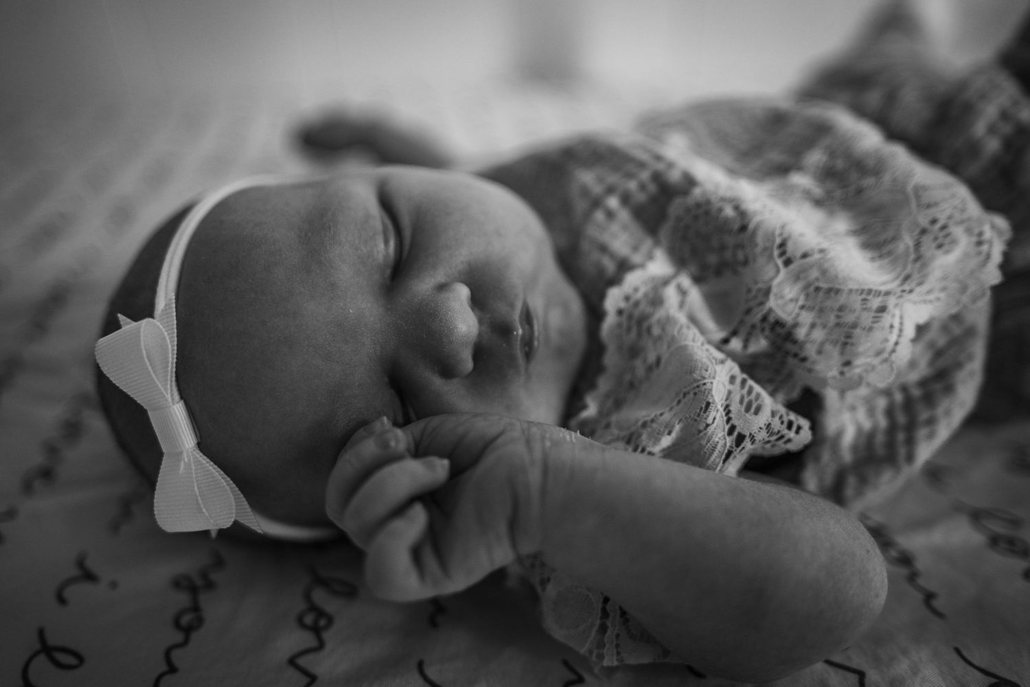 Sleeping infant wrapped in lace blanket captured in black and white photography.
