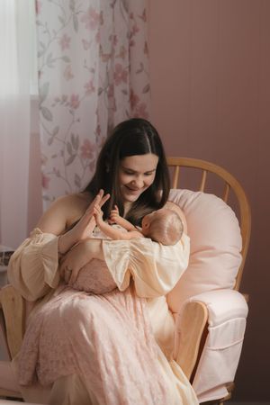 A tender moment of bonding between parent and baby in a cozy nursery chair with floral curtains in the background.