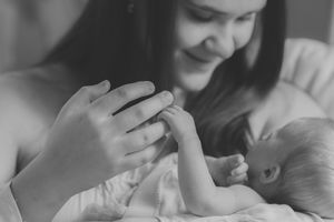 A tender black and white moment of parent and baby holding hands while sharing a joyful connection.