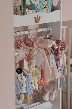 Baby clothes hanging on white closet rod with adorable pink and blue outfits arranged neatly in a nursery.