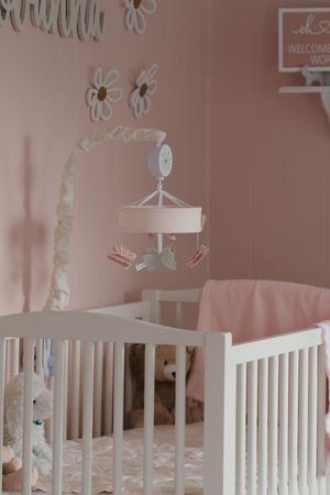 White baby crib with mobile and pink walls decorated with flower decals in a dreamy nursery setting.