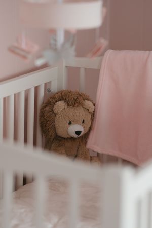A plush brown lion toy rests inside a white baby crib with pink bedding and decor.