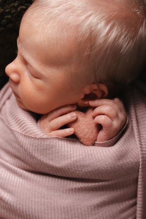 Peaceful sleeping newborn baby wrapped in soft pink knit swaddle blanket.