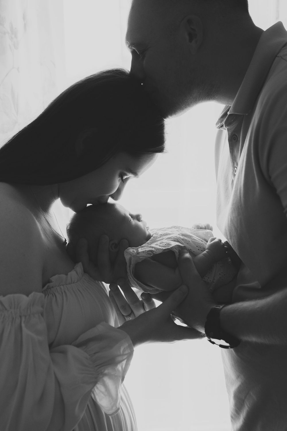 Black and white intimate portrait of parents tenderly gazing at their newborn baby.