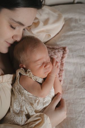 Tender moment of mother and newborn baby resting together on white bedding.