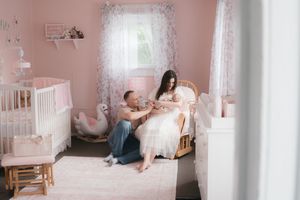 A cozy pink-walled nursery with white crib, rocking chair and soft decor showing a tender moment.