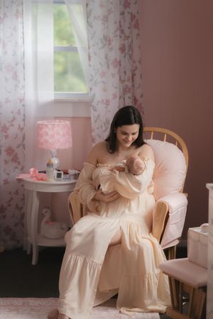 A serene nursery scene with peachy pink floral wallpaper, a rocking chair, and soft natural light from the window.