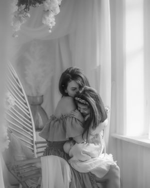 Black and white dreamy portrait by window with soft lighting, flowing dress and palm leaf shadow in ethereal scene.
