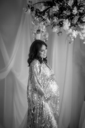 A black and white maternity photo showcasing an expectant figure in a sparkly gown under floral decor in the Hudson Valley,NY.